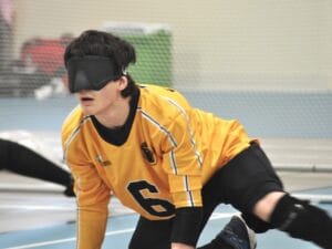 A goalball layer in a yellow jersey crouches in front of the net.